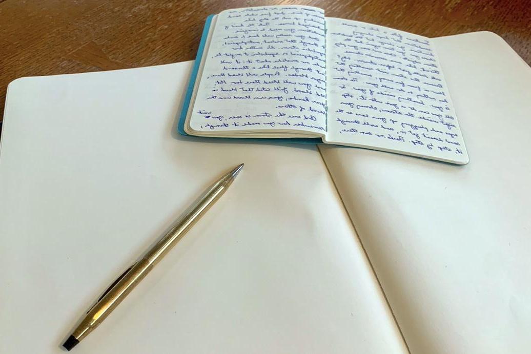 一个写着字的笔记本用一支笔放在空白的笔记本上面.